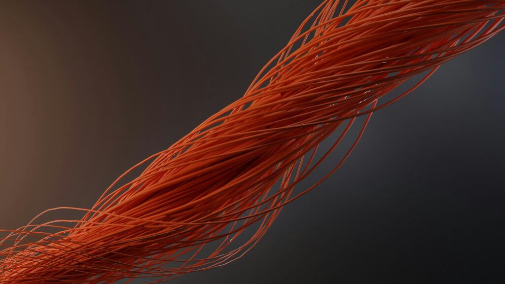 An abstract 3D render of thousands of thin, vibrant orange strings or fibers intertwined and bundled together, diagonally crossing a dark gradient background. This visualizes concepts like neural networks, high-density synthetic fiber durability, and complex interconnected systems.